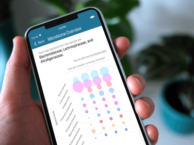 A photograph shows a hand holding an iPhone. The top of the illuminated screen reads 'IBD Tracker' and then shows text that reads 'Please submit a sample'. Below this, a menu appears with two options: 'My Reports' and 'My Food Log'.